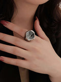 Elegant vintage ring watch on hand with dark nail polish, showcasing intricate dial design and stylish silver band.