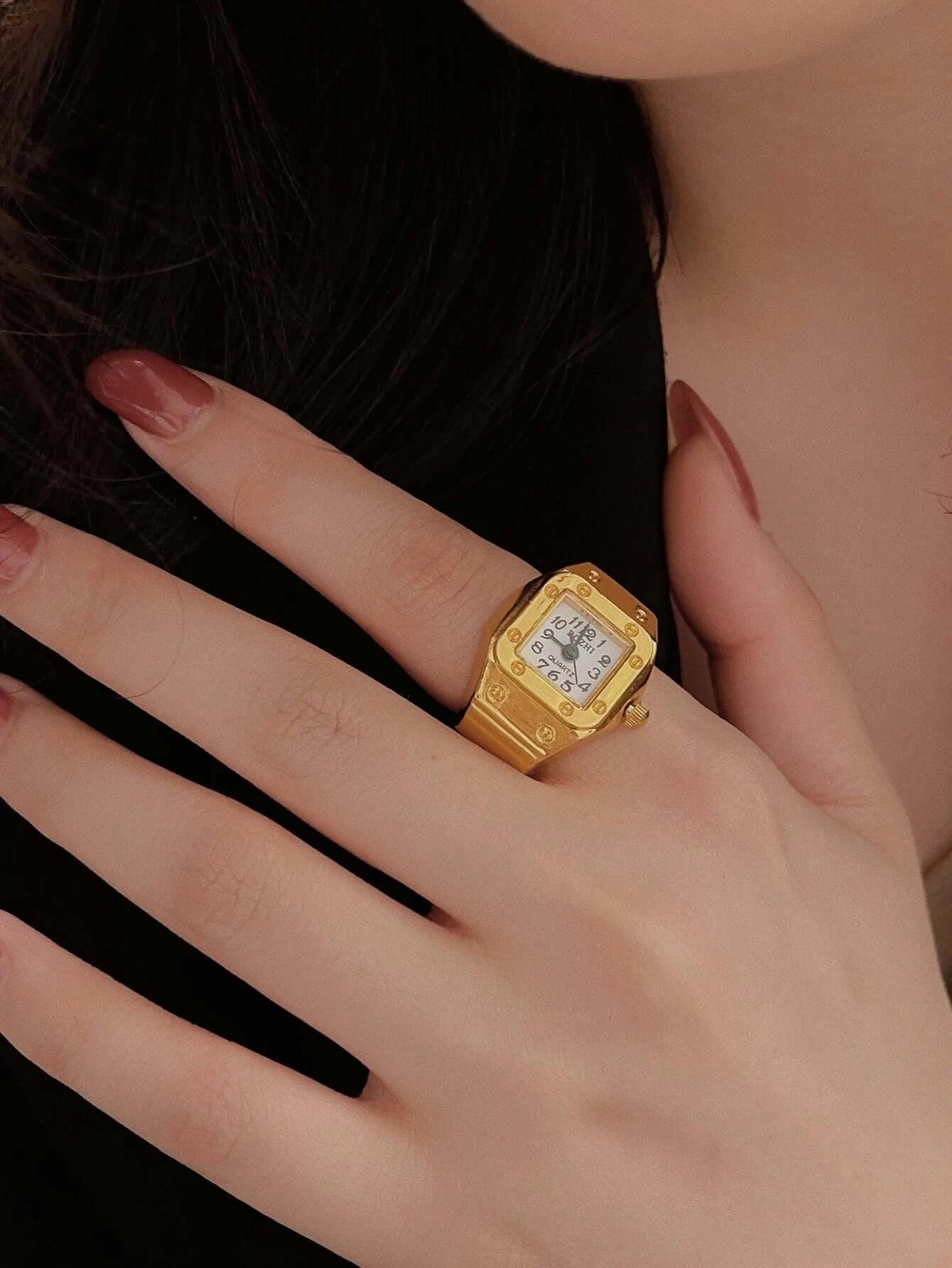 Gold vintage ring watch on a hand with red nails, featuring a square dial and intricate detailing.